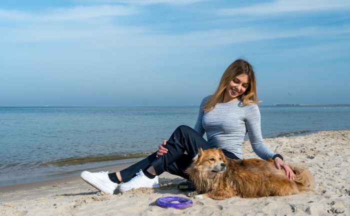Woman enjoying a sunny day at Kołobrzeg beach with her dog, capturing a perfect seaside moment.