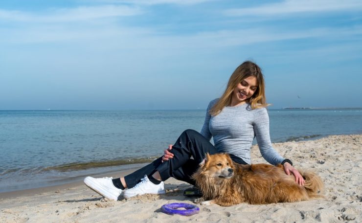 Woman enjoying a sunny day at Kołobrzeg beach with her dog, capturing a perfect seaside moment.