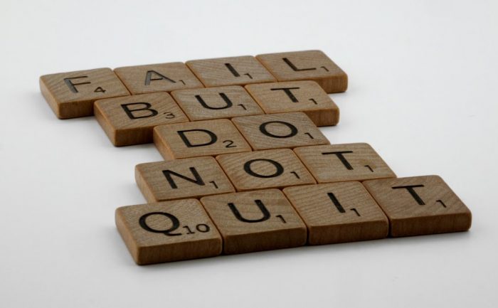 Wooden Scrabble tiles arranged to spell 'Fail but do not quit,' inspiring determination.