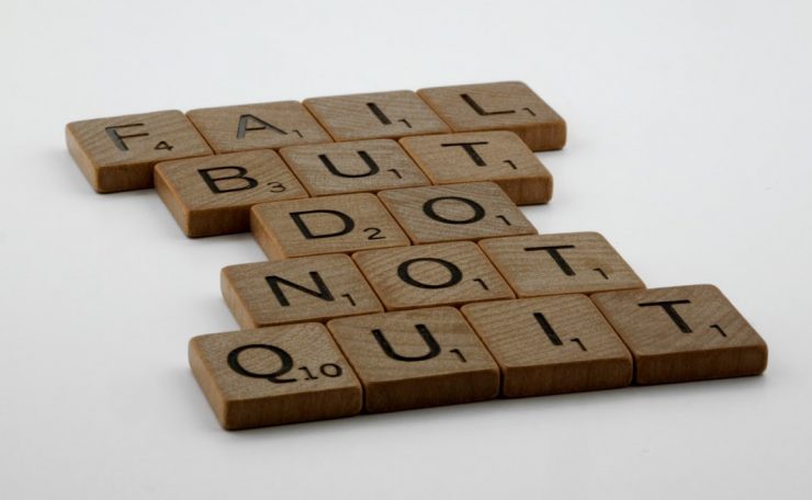Wooden Scrabble tiles arranged to spell 'Fail but do not quit,' inspiring determination.